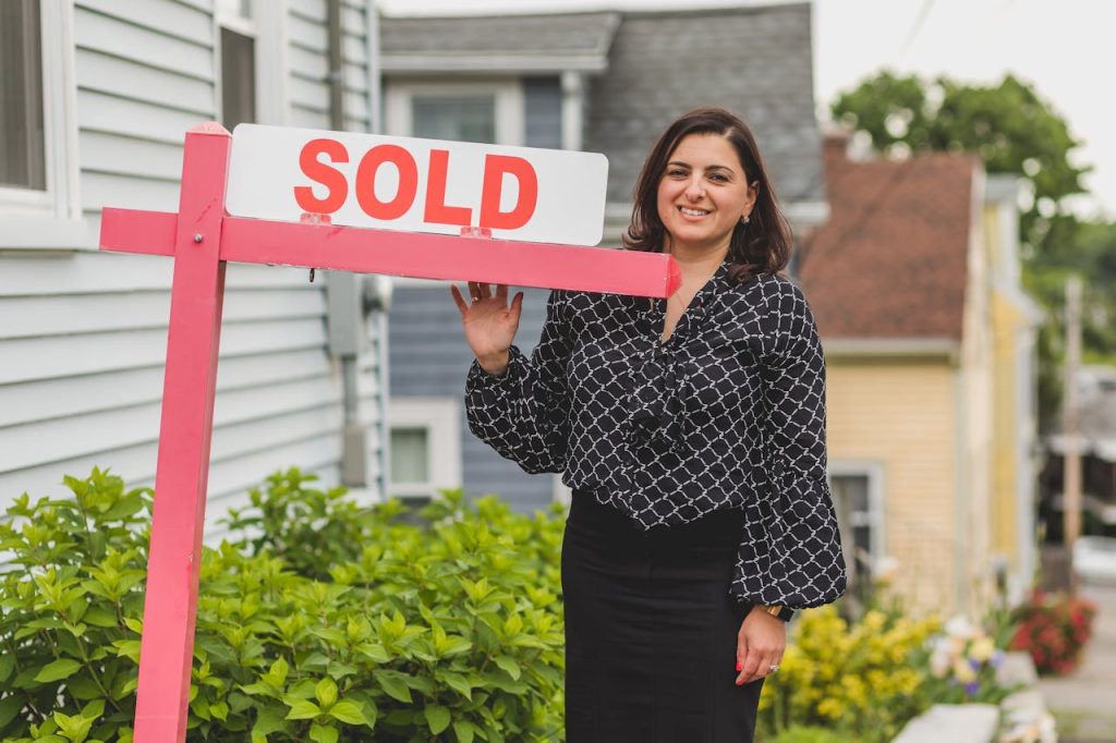 The Art of Drawing Readers In: Your attractive post title goes here Smiling real estate agent standing outdoors with a sold sign, symbolizing success and achievement in property sales.